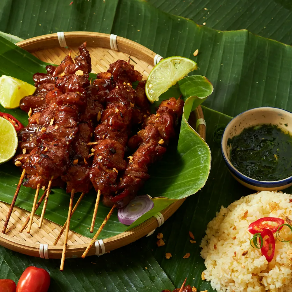 Grilled satay skewers glazed in sauce on a banana leaf with lime and chili, a restaurant signature dish